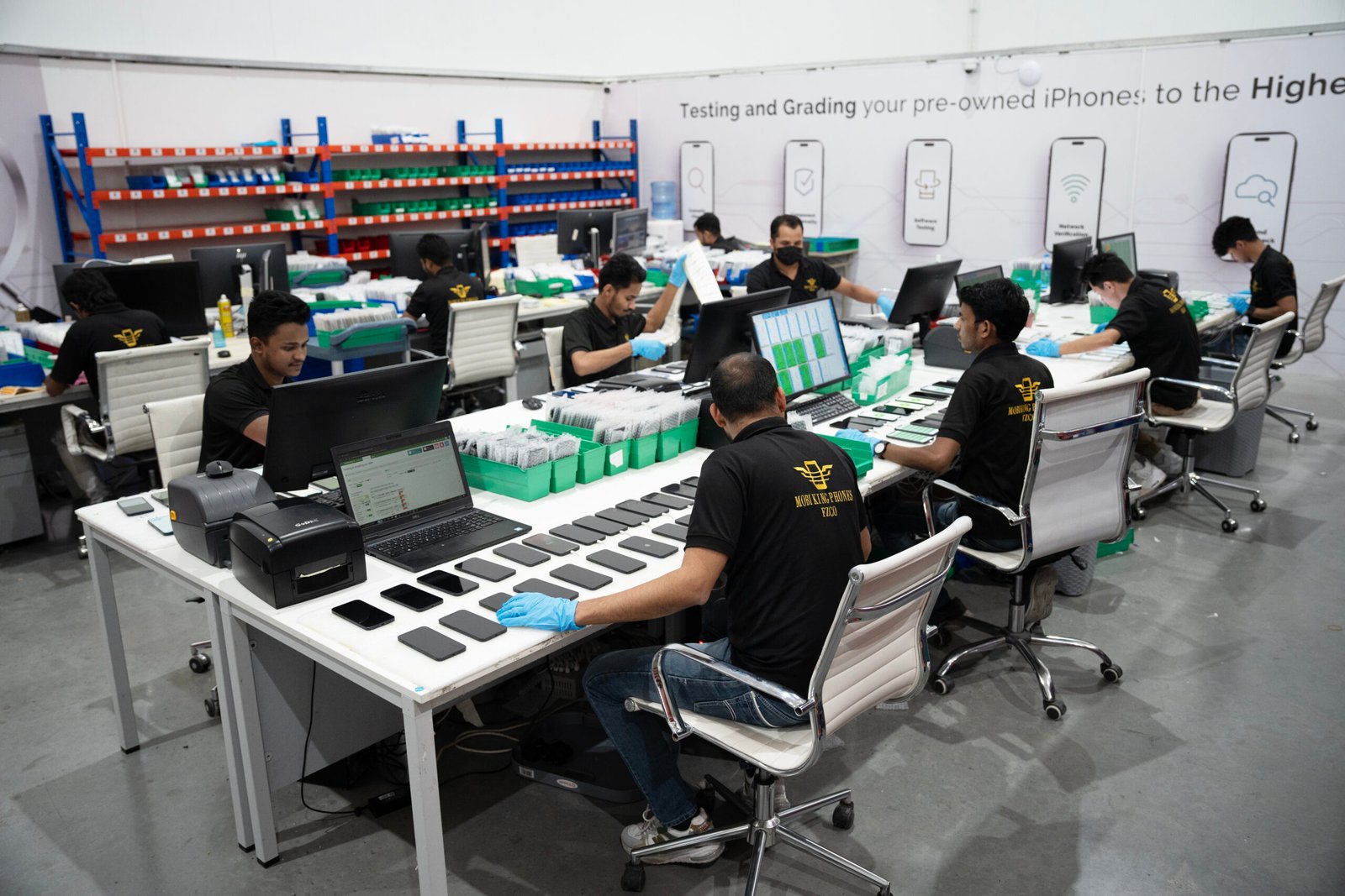 MOBIKING Phones FZCO team testing and grading used iPhones in a wholesale facility.